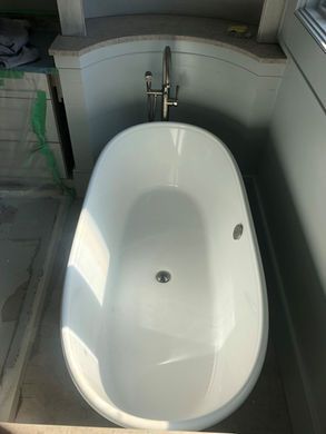 White freestanding bathtub beneath a wall-mounted faucet in a tiled bathroom