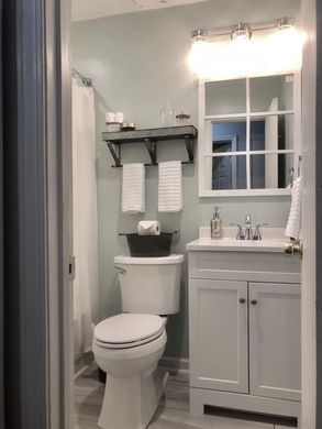 Small bathroom with toilet, white vanity, mirror, and black towel shelf above the toilet.