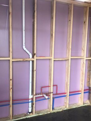 Framed wall with purple insulation, exposed studs, and plumbing pipes during construction