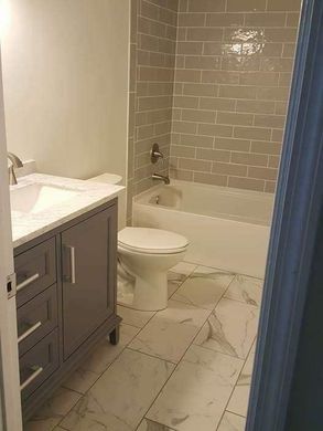Small bathroom with vanity, toilet, and bathtub with gray tile walls and white marble floor.