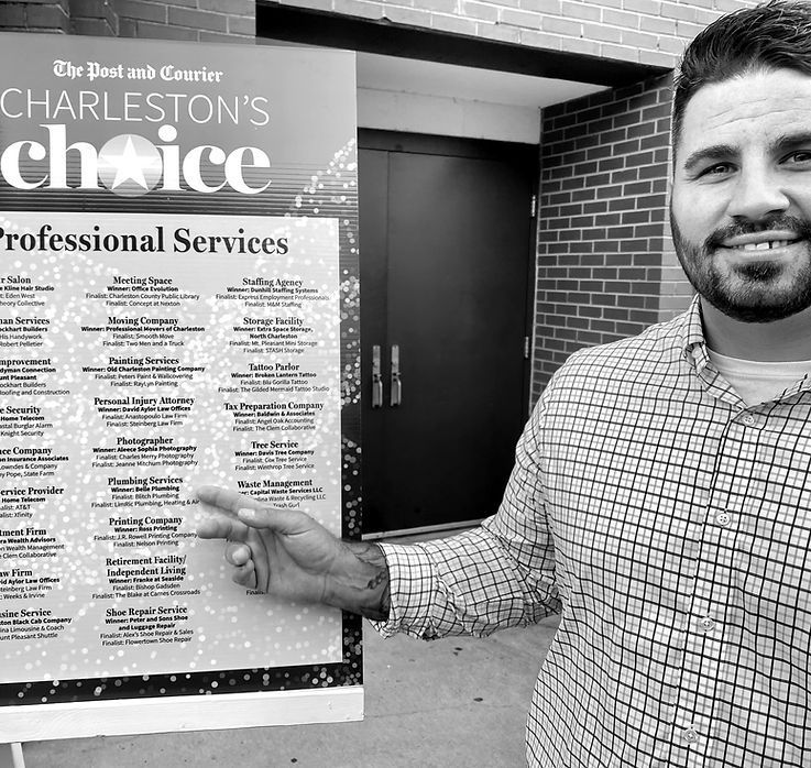 Man points to a “Charleston’s Choice” Professional Services award poster outside a building.