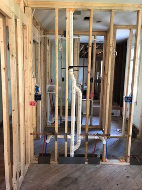 Framed interior wall with exposed plumbing pipes and electrical wiring in a room under construction