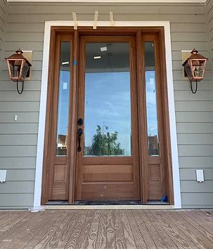Front porch with a wooden double front door, flanked by lanterns and gray siding.