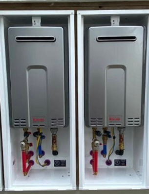 Two wall-mounted tankless water heaters with red, blue, and yellow pipes in white cabinets.
