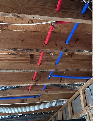 Ceiling joists with red and blue PVC pipes running through an unfinished room