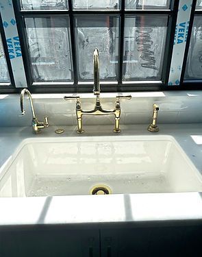 White farmhouse sink with brass faucet on a windowsill in a bright kitchen