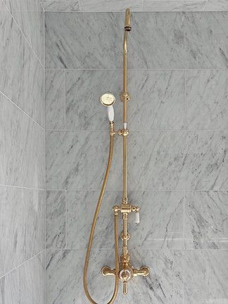 Gold shower fixture with handheld sprayer against a gray marble-tiled wall