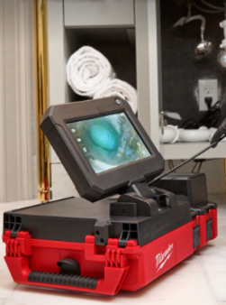 Red-and-black inspection device with a tilted screen on a tabletop, with a rolled white towel behind it.