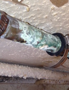 Corroded metal pipe with green-blue rust stains near a ceiling junction
