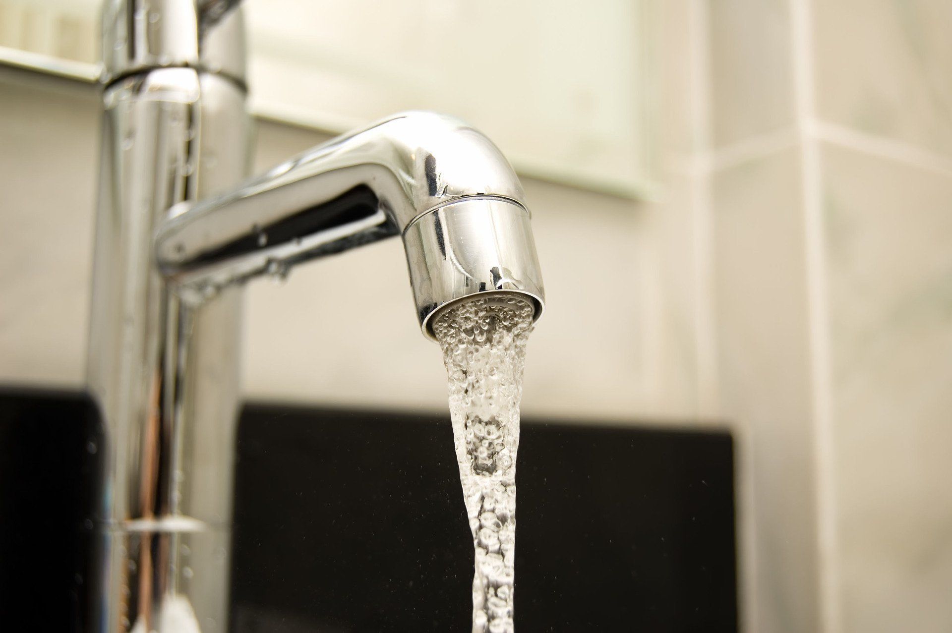 Close-up of a chrome faucet with water flowing from the spout, in a bathroom.