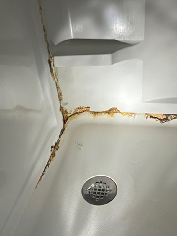 Cracked and damaged white shower stall with rusty sections near a drain.