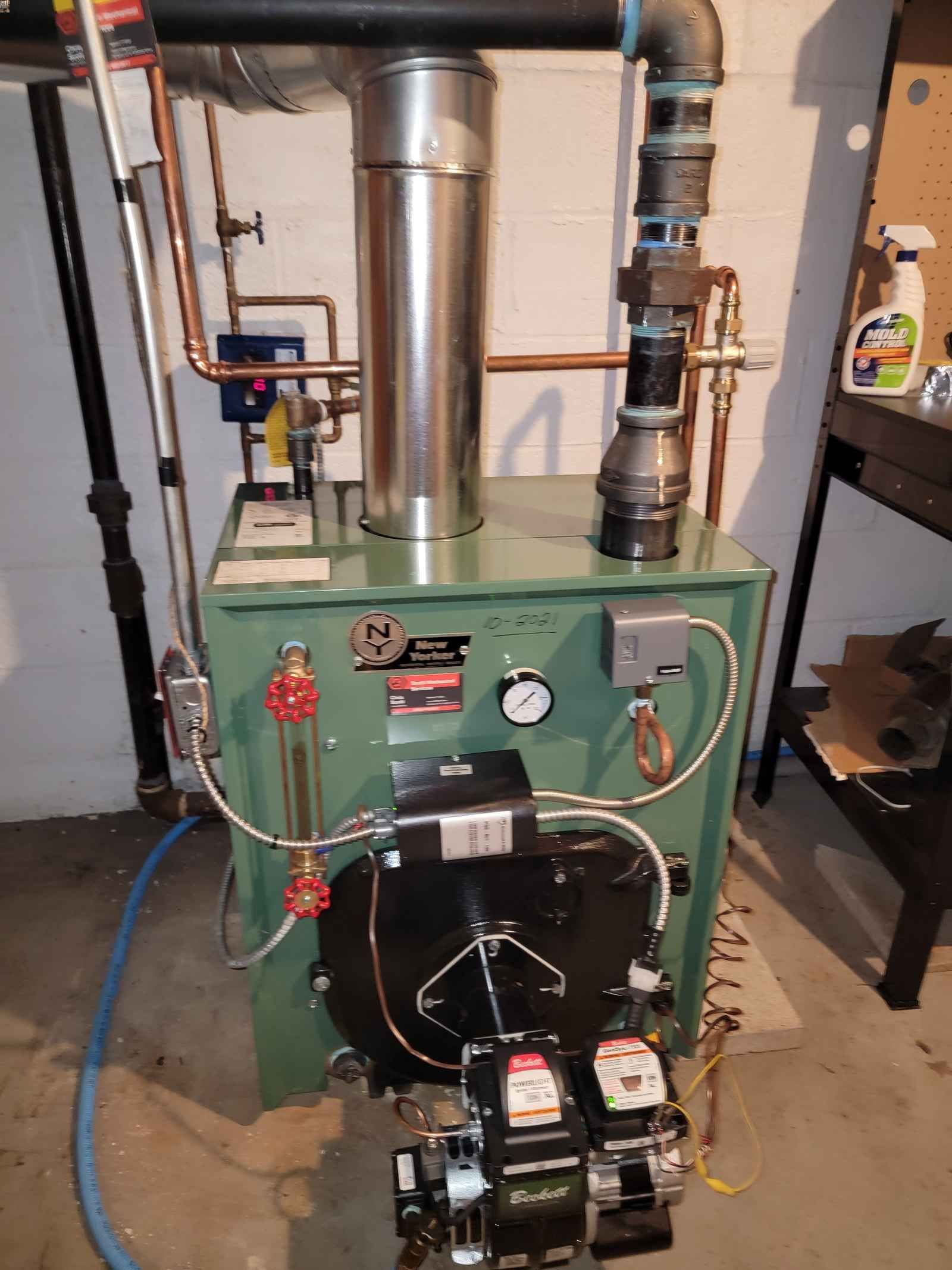 A green boiler is sitting in a basement next to a hose.