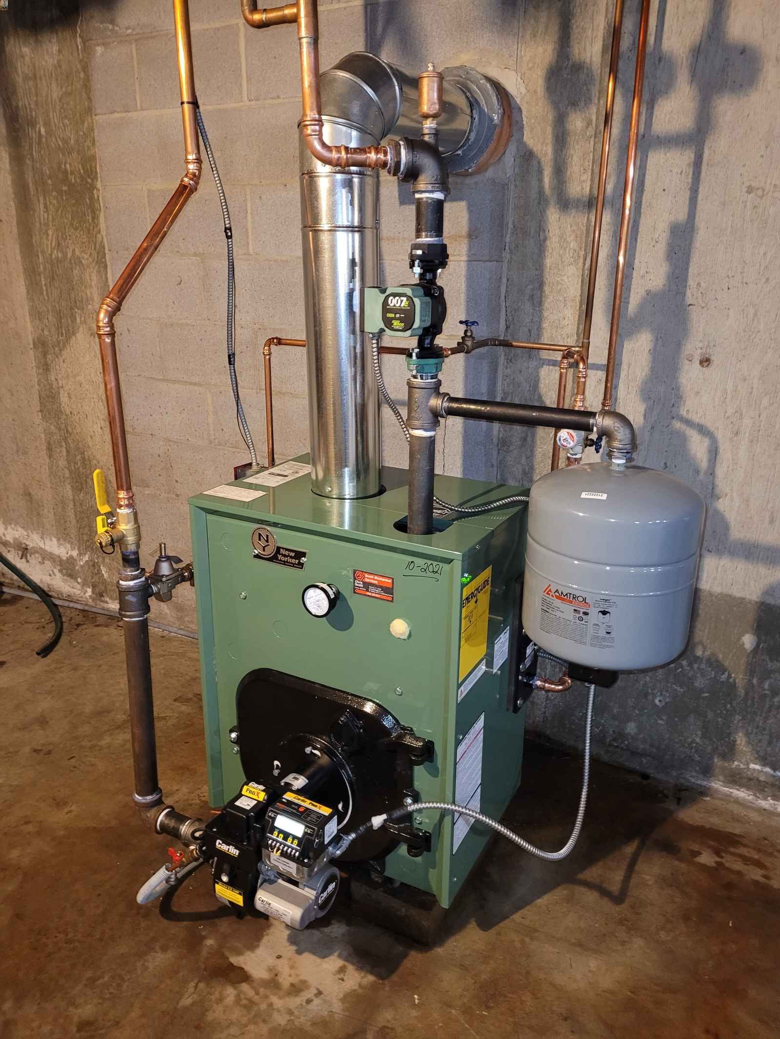 A green boiler is sitting in a basement next to a brick wall.