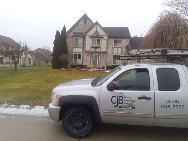A silver work truck with the CJB company logo parked on a street in front of a residential house on a cloudy day.