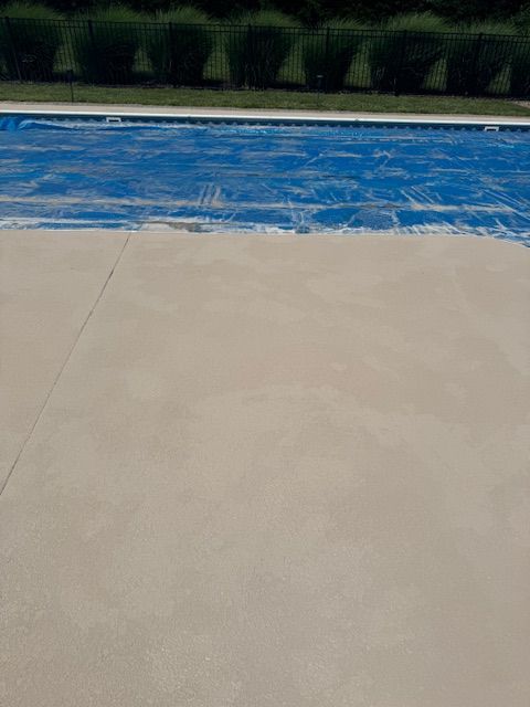 Beige concrete patio area with a blue pool cover; green foliage in the background.
