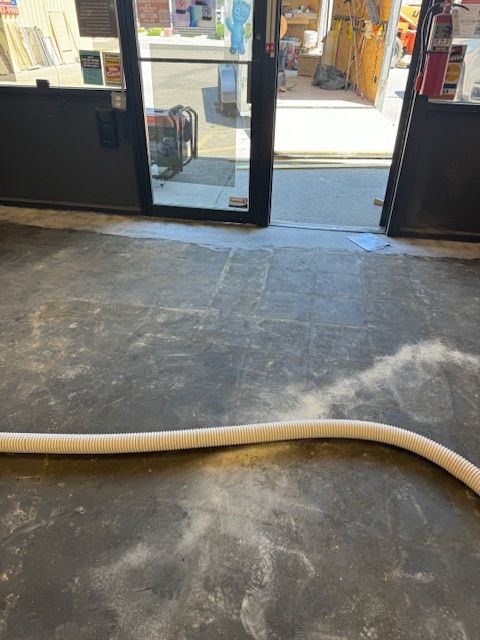 A doorway with an open entrance, concrete floor scattered with dust, and a white hose.