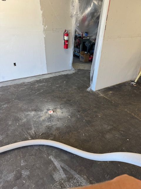 Interior construction site with gray concrete floor, unfinished drywall walls, and a fire extinguisher.