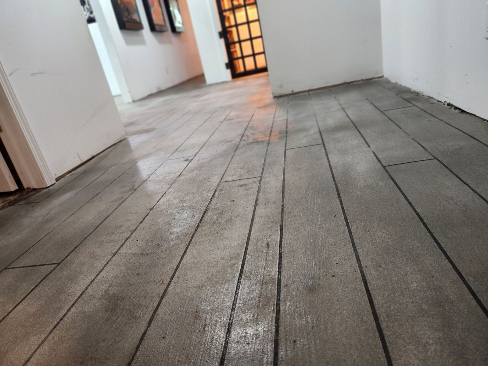 Gray wooden plank floor in a hallway, leading towards a door with glass panels.