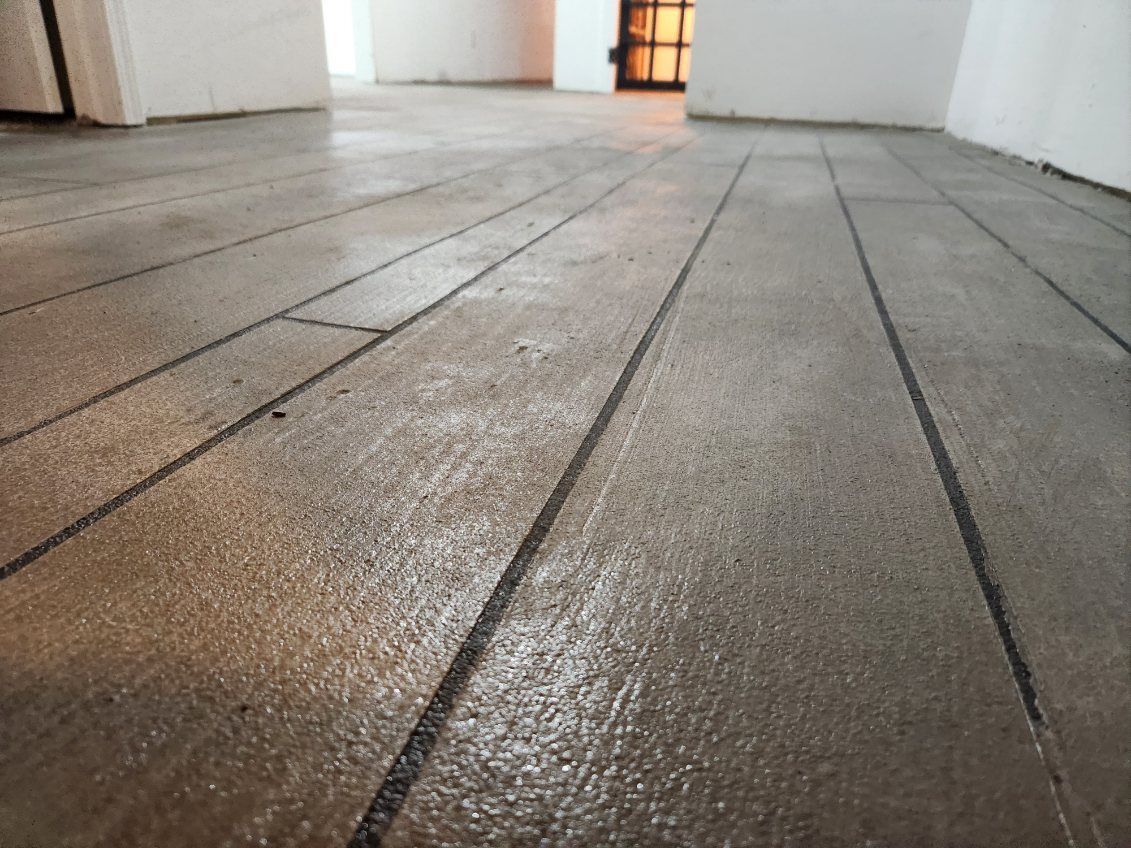 Close-up of a weathered, gray wooden plank floor with dark grout lines, in a room with white walls.