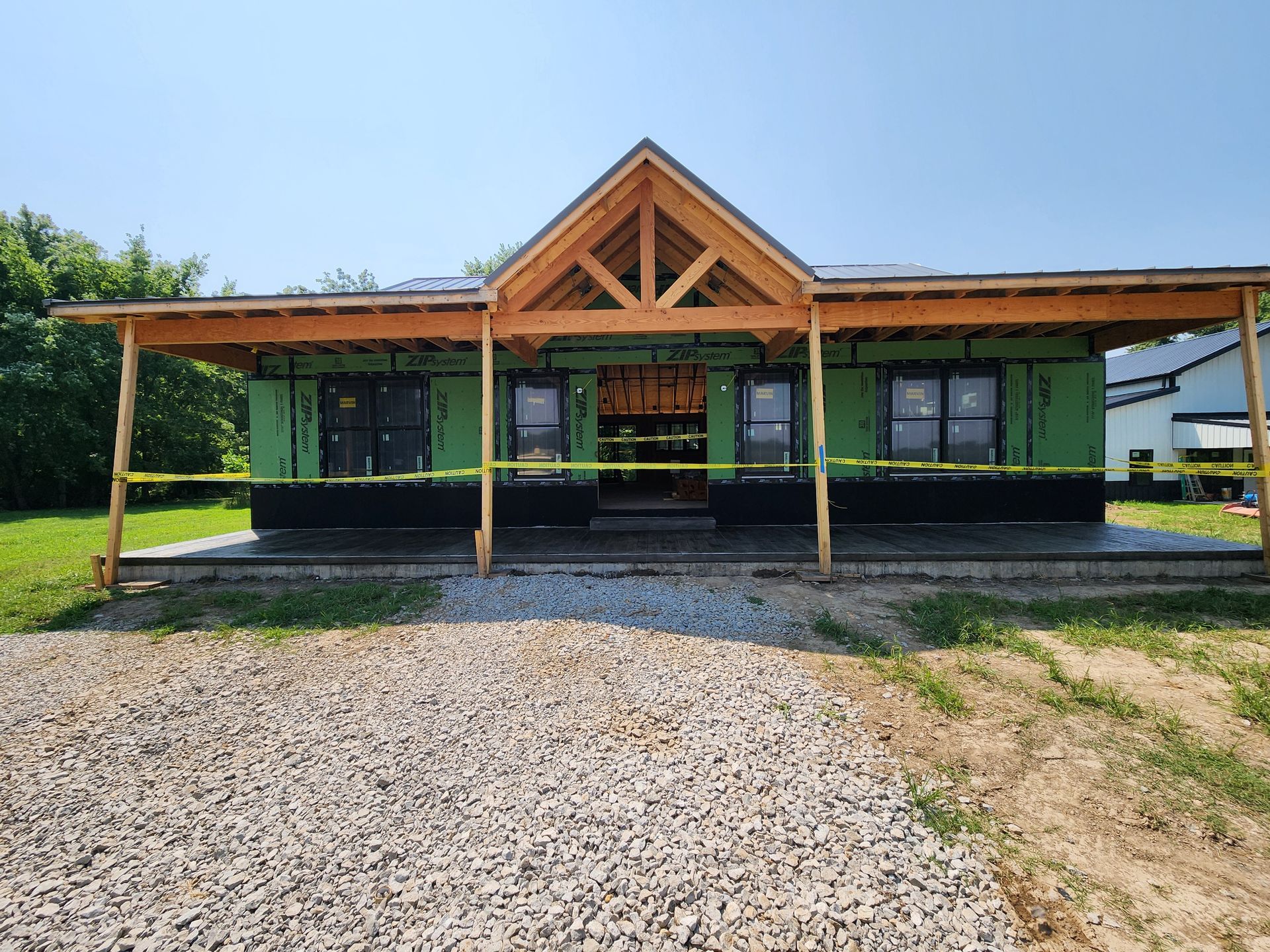 New house under construction with green insulation, wooden beams, and a gravel driveway.