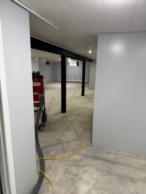 Gray-walled basement renovation in progress, featuring black support beams and concrete floor.