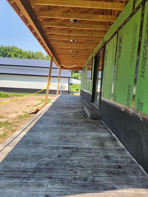 Gray stamped concrete porch under construction with wooden ceiling, building with green sheathing.
