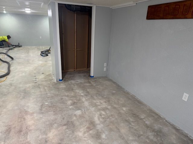 Basement with gray walls, concrete floor, doorway with closed doors, and a person working with vacuum hoses.