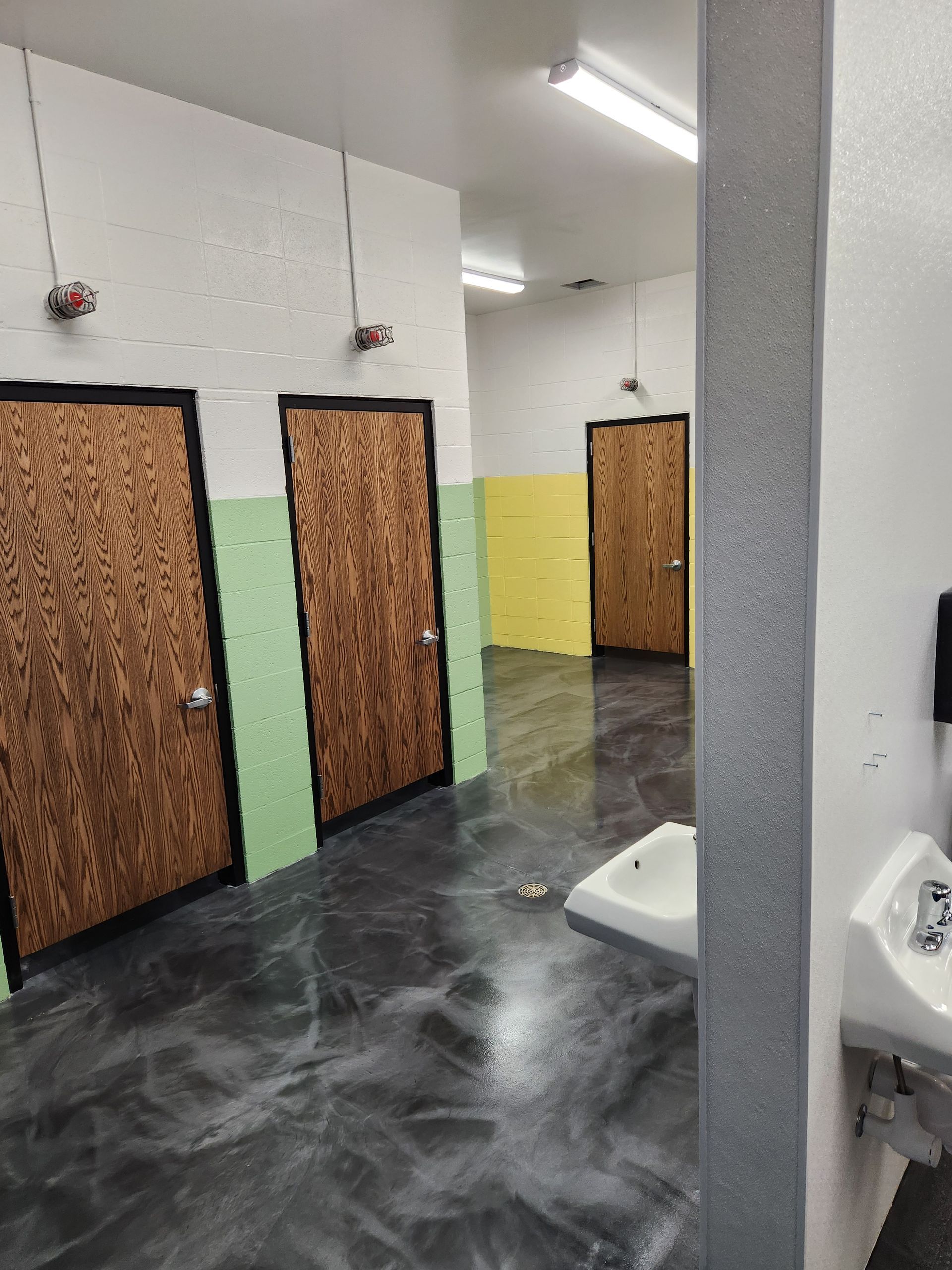Public restroom with dark floor, brown doors, and light green and yellow accents.