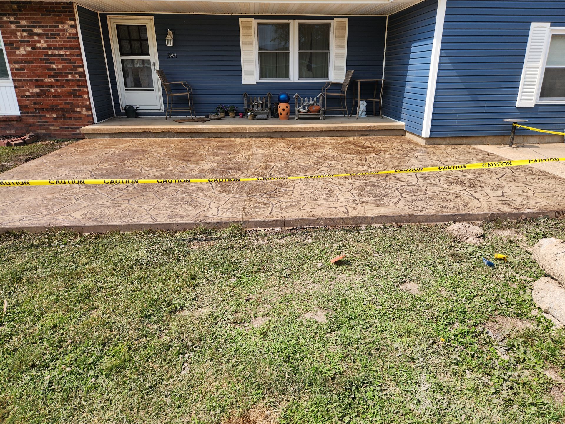 Stamped concrete patio in front of a blue house with caution tape.