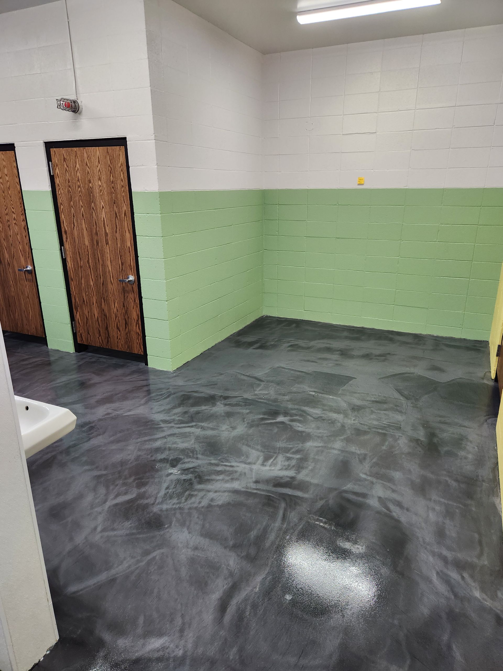 Empty bathroom with dark floor, green and white walls, two wooden doors, and a sink.