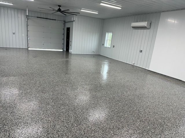 Spacious, empty garage with epoxy floor, closed overhead door, and air conditioning unit.