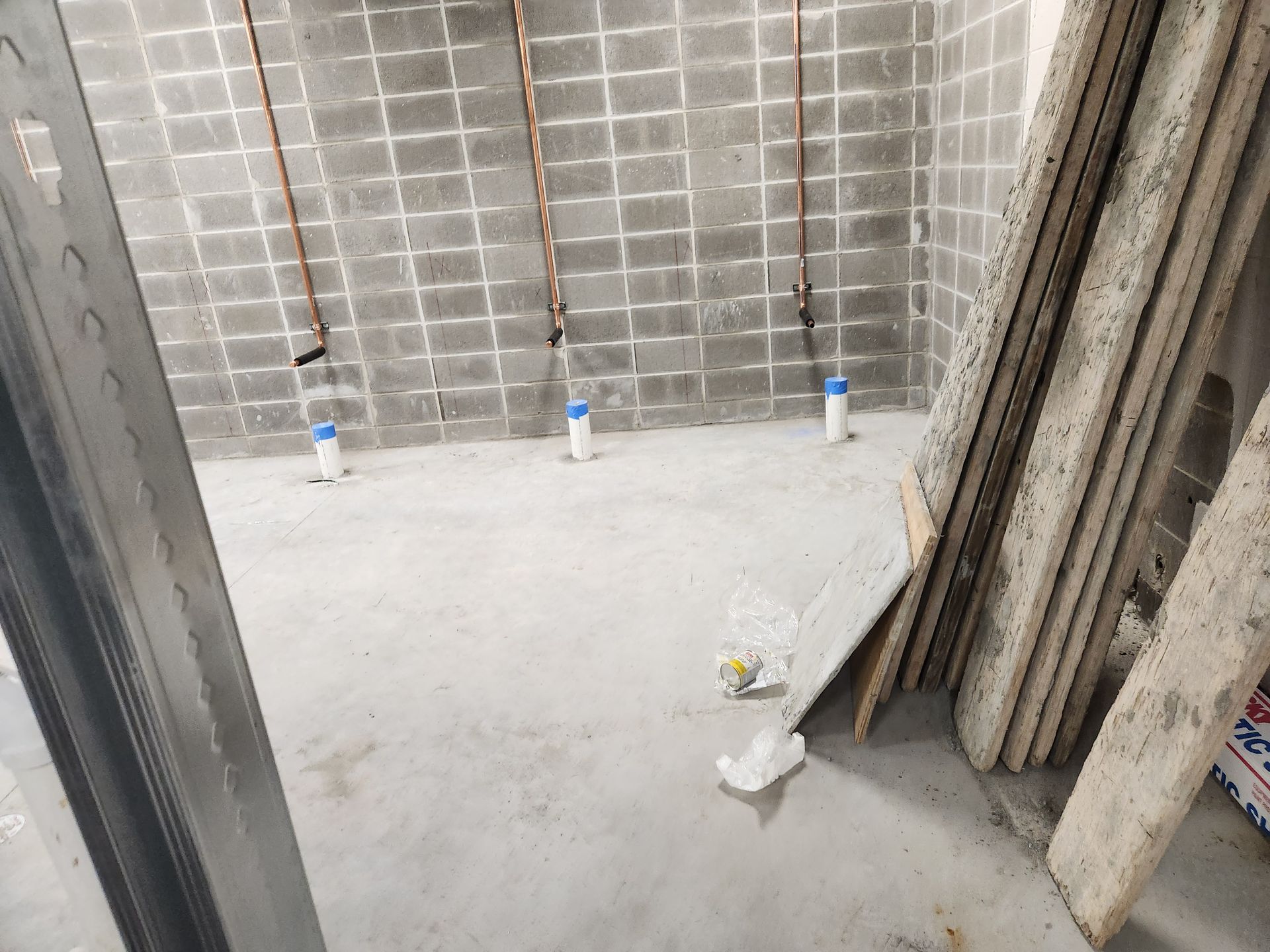 Interior view of a bathroom under construction with plumbing pipes and concrete walls.