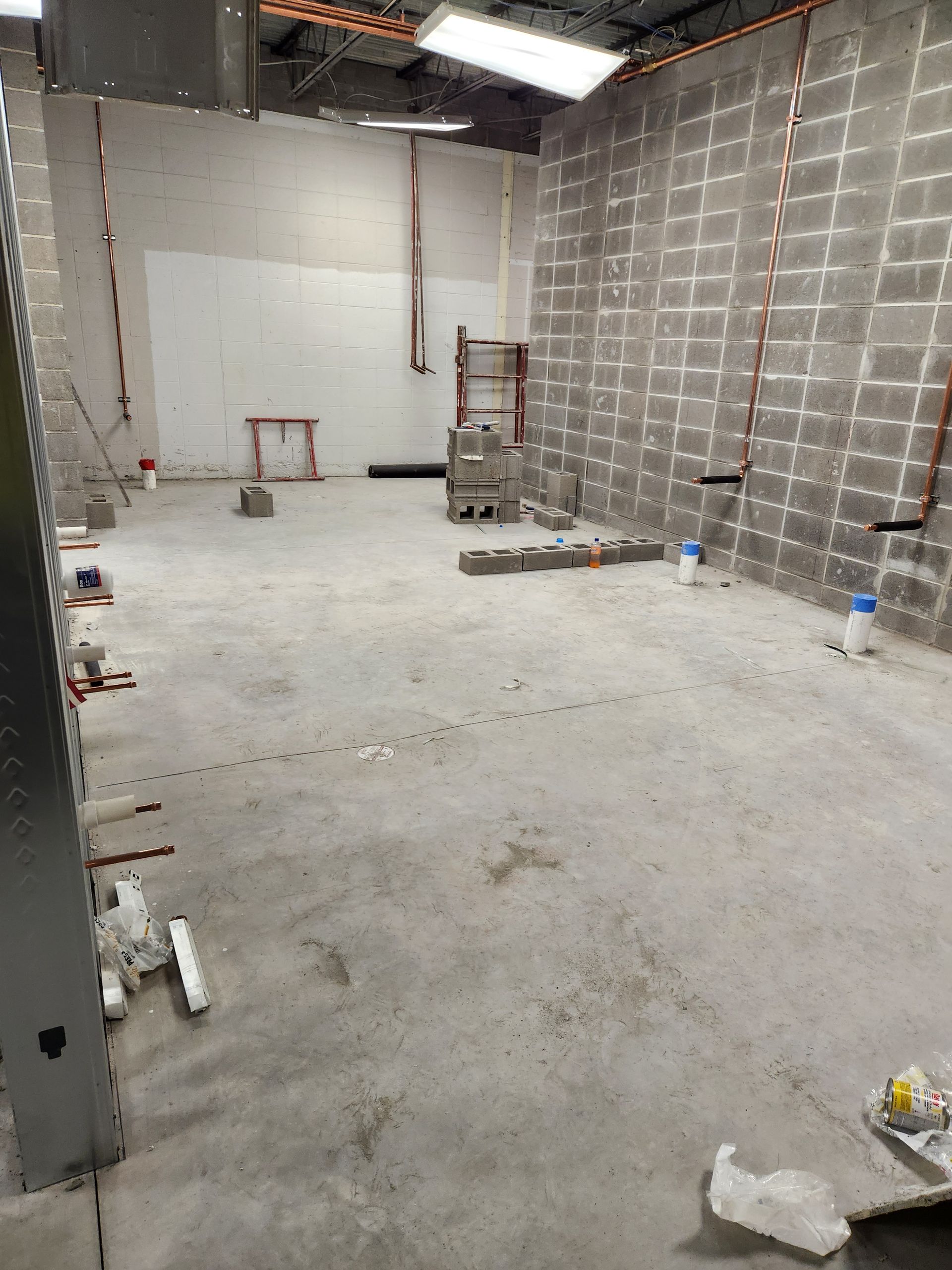 Construction site interior, concrete floor, block walls with exposed copper pipes.