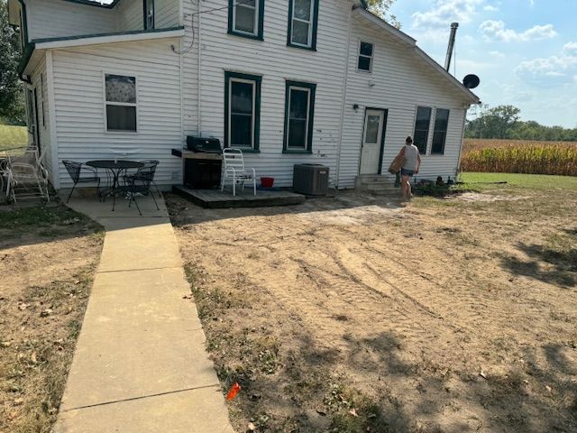 A white house with a concrete walkway and a person walking toward the back door, next to a field.