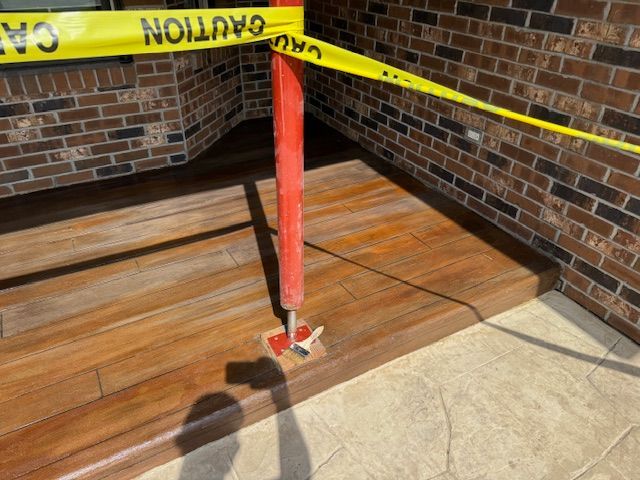 Yellow caution tape and a red post block access to a wooden porch with brick wall.