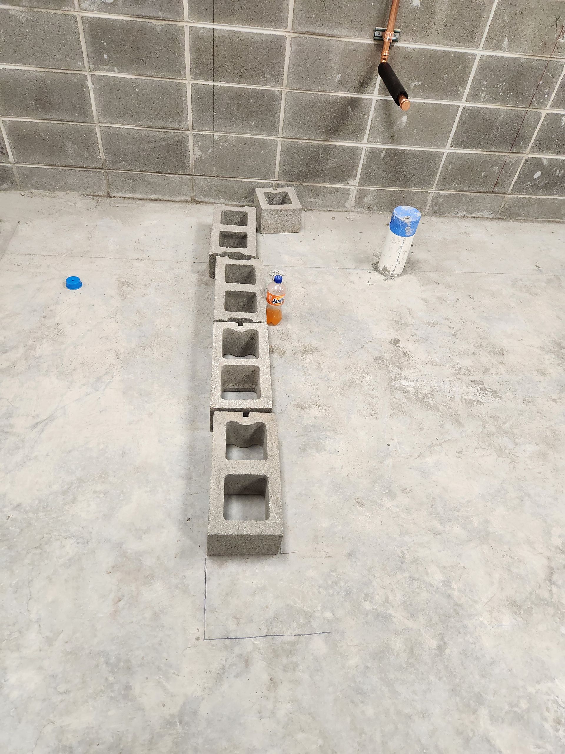 Concrete blocks arranged in a line on a concrete floor near a partially constructed wall.