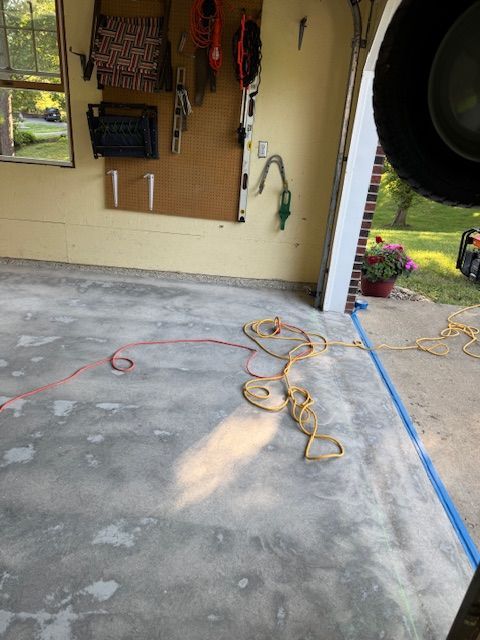 Garage interior with a gray concrete floor, extension cords, and tools mounted on the wall.