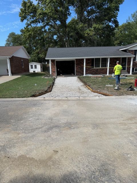 A house with a gravel path leading to the garage. A person in a yellow shirt stands near the driveway.