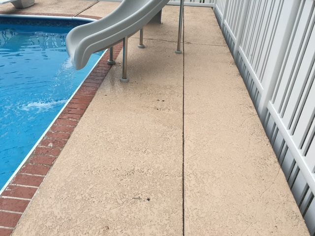 Poolside concrete walkway with a water slide and white fence.
