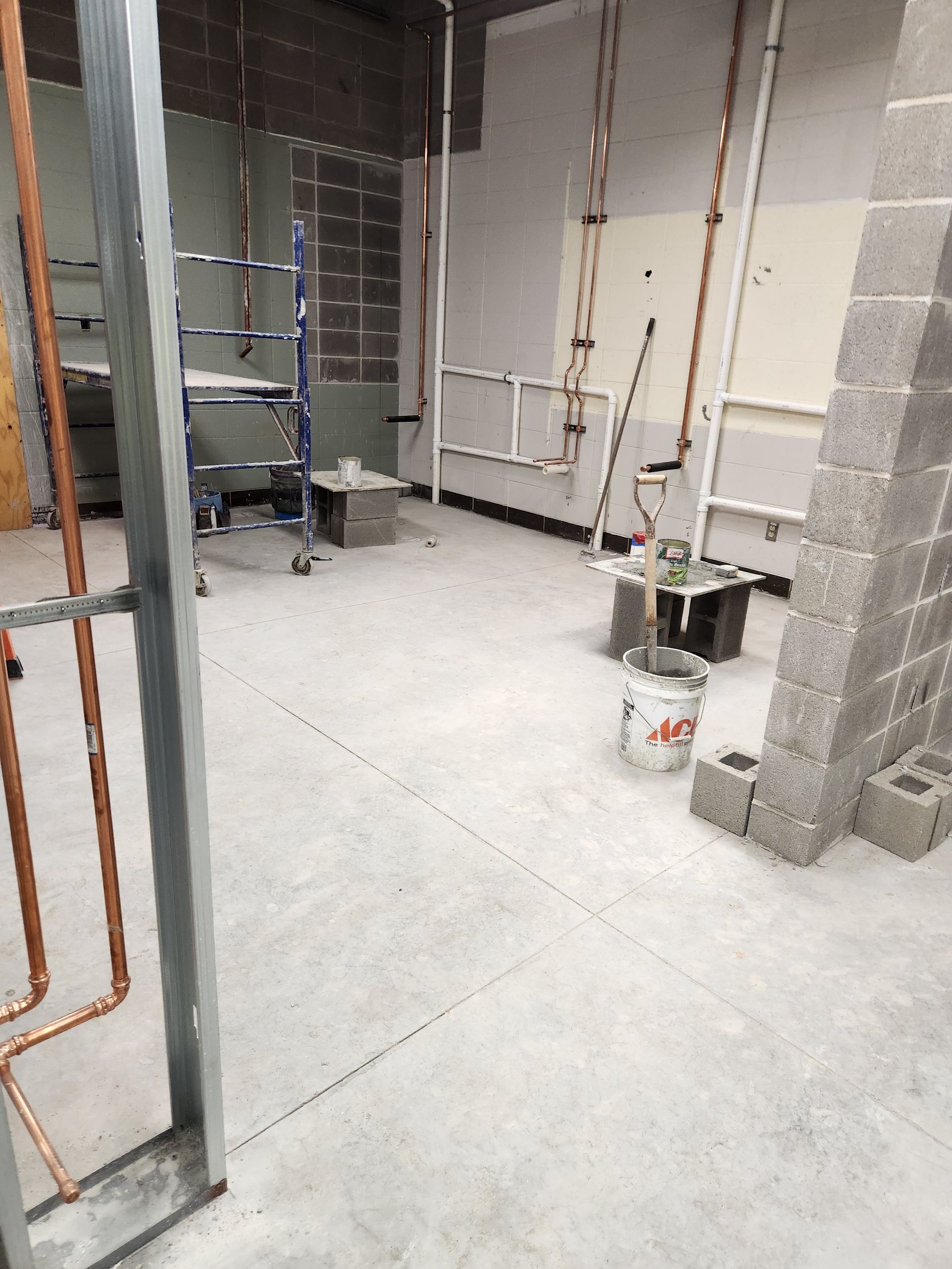 Construction site interior with exposed pipes, block walls, and unfinished flooring.