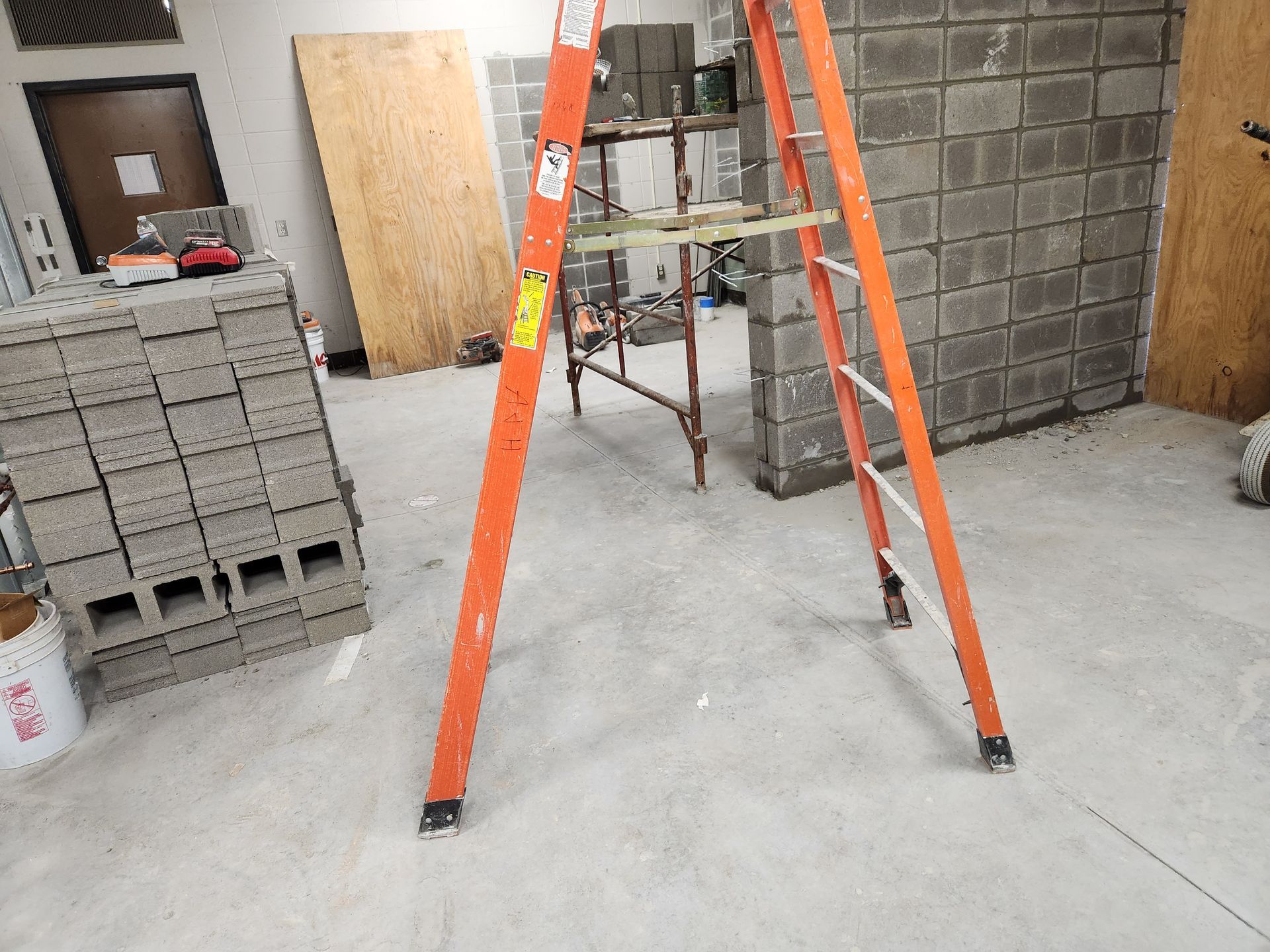 Orange ladder in a room with cinder block walls and concrete floor, construction site.