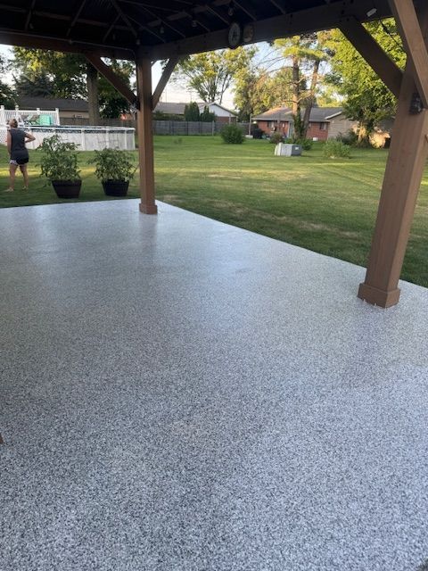 Patio with speckled light gray coating under a gazebo. Person standing on the grass.