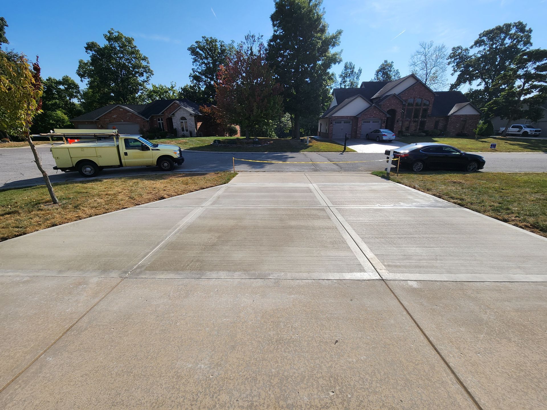 Concrete driveway leading toward houses; a yellow truck and black car are parked on either side.