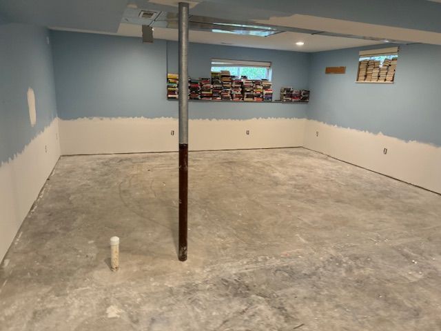 Basement room with concrete floor, blue walls above white wainscoting, and a support pole in the center.