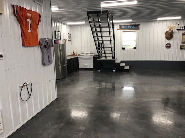 Garage interior with concrete floor, metal walls, kitchen area, staircase, and sports memorabilia.