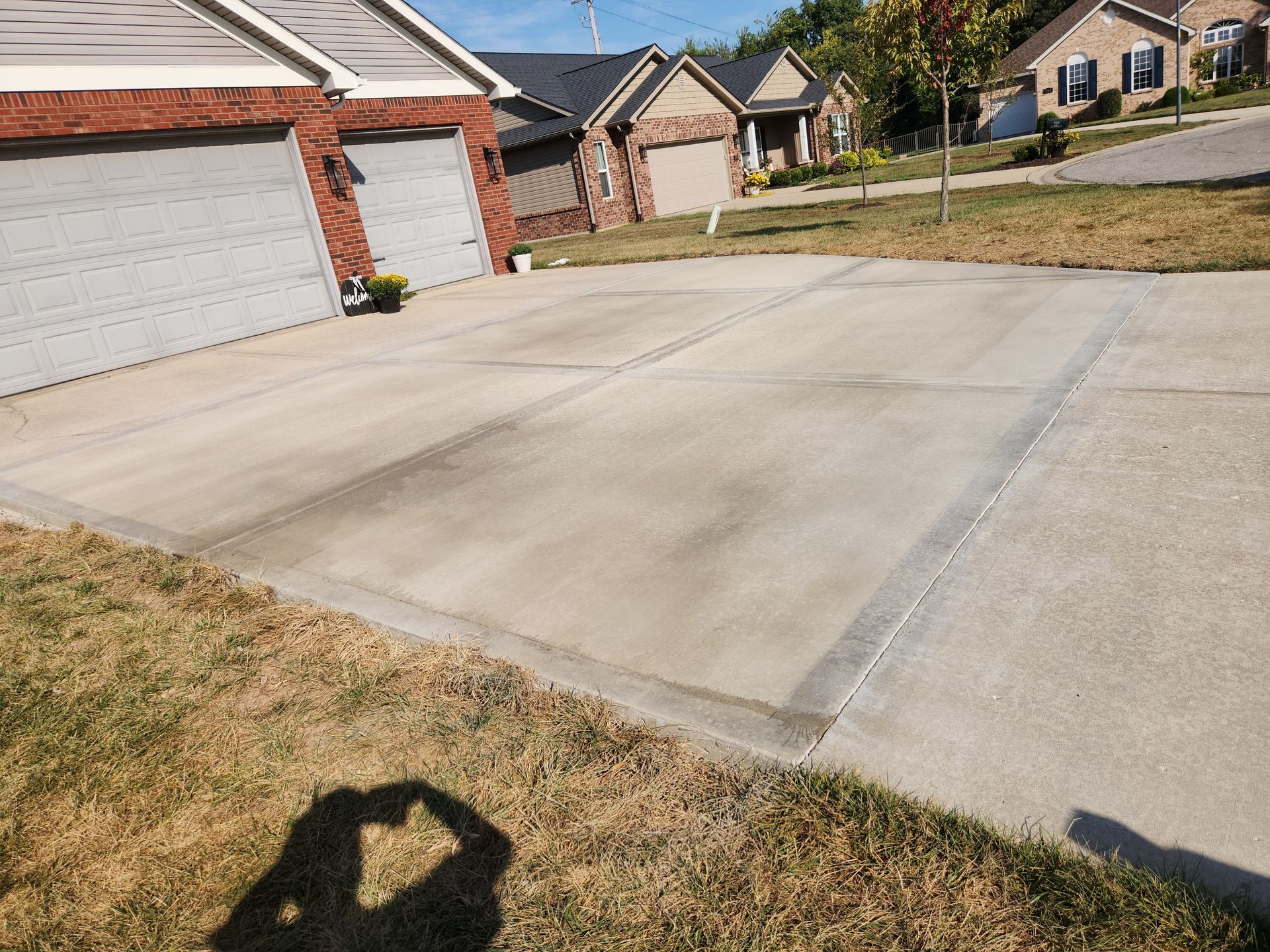 Concrete driveway with two garage doors and residential houses in the background. Sunny day.