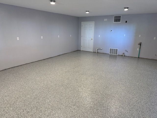 Empty room with gray walls and speckled epoxy floor; white door and vent visible.