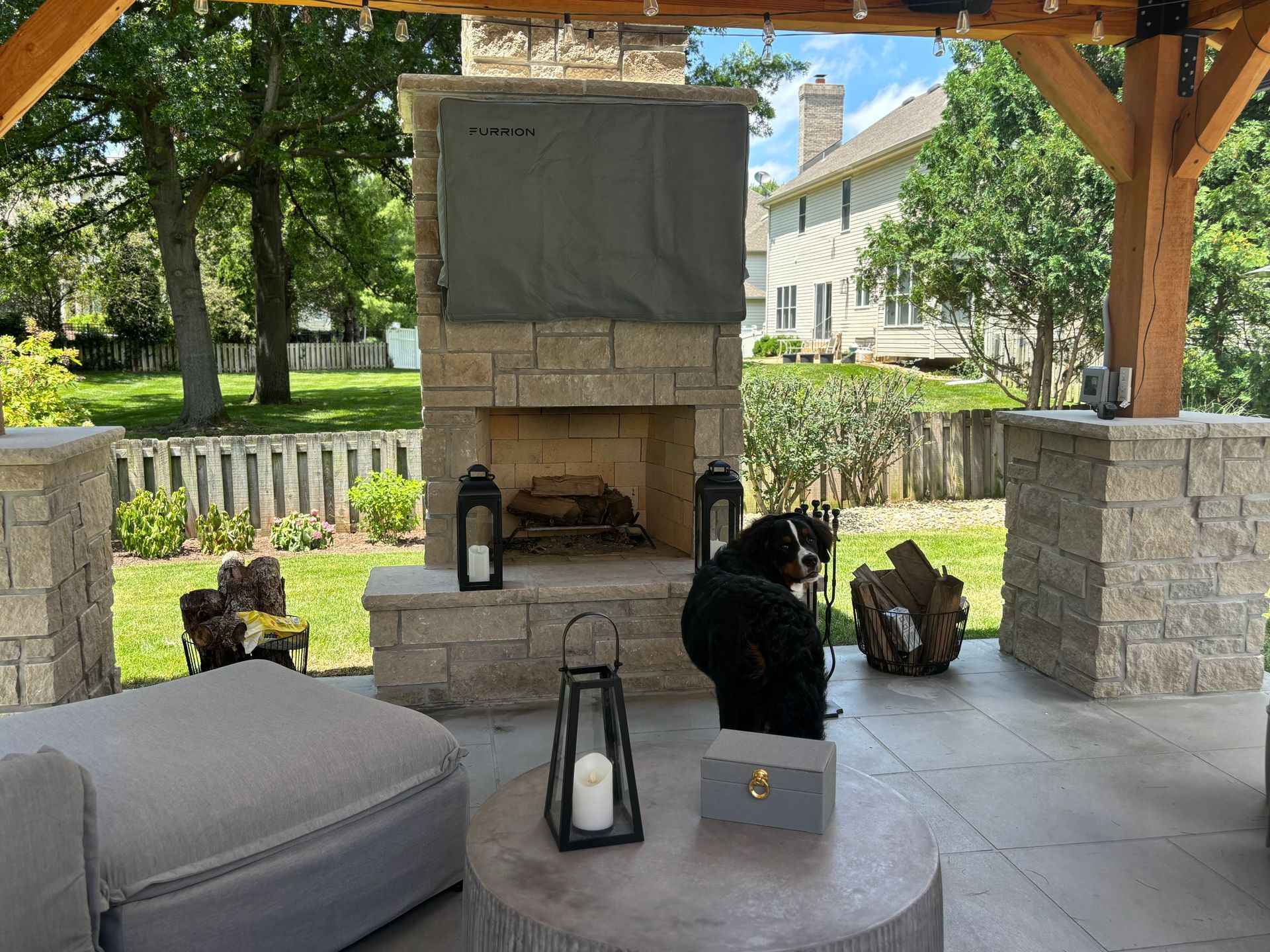 Outdoor fireplace with a TV cover, a seated bear statue, and patio furniture.