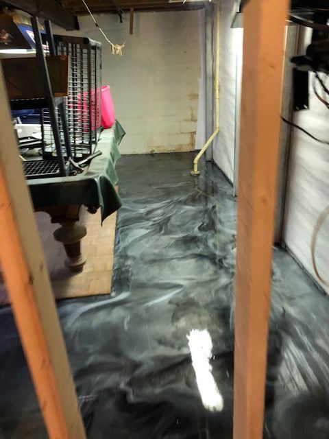Basement with black and silver epoxy floor, unfinished walls, pool table, and wooden beams.
