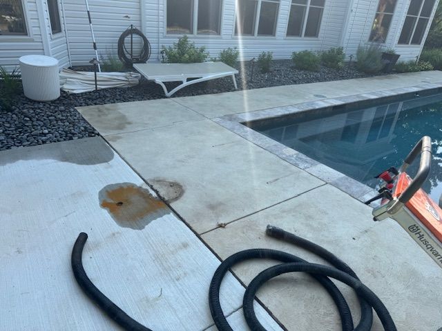 Concrete pool deck with hose, staining, and a chainsaw. A white house is in the background.